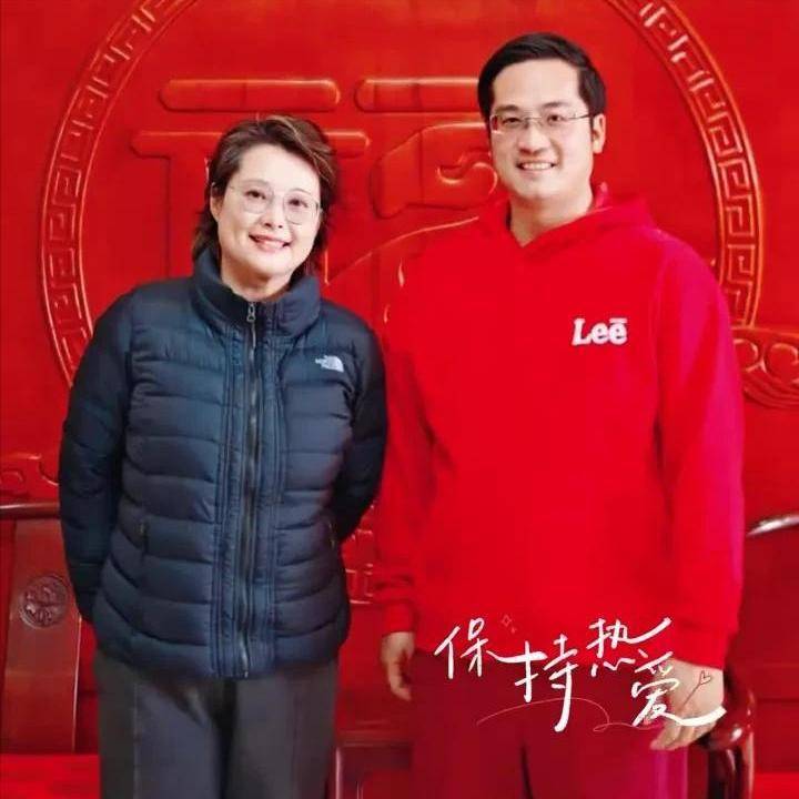 下半身穿了深红色休闲裤,一身的红红火火,还戴着眼镜,单手竖起大拇指